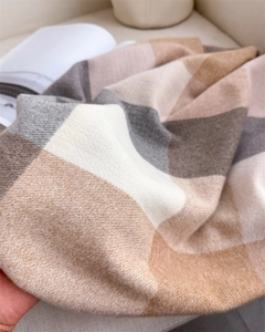 Gros plan sur la texture épaisse d'une écharpe à carreaux crème, gris et kaki