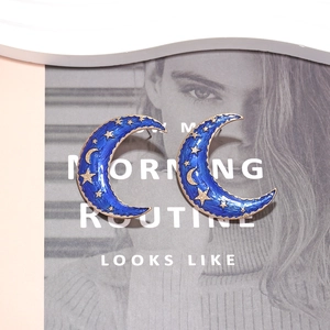 Boucles d'oreilles lune dorées vintage avec émail bleu et motif d'étoiles sur fond magazine