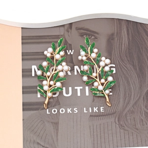 Elegant gold leaf earrings with green enamel and white pearls on fashion magazine