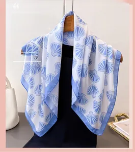 Detail of silk-like square scarf featuring blue seashell prints on white fabric