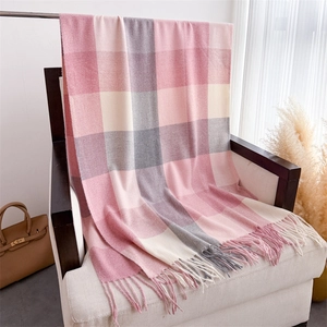 Détail de l'écharpe à carreaux rose et gris avec franges sur un fauteuil blanc
