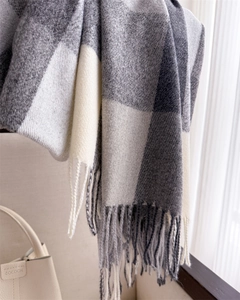 Détail de l'écharpe à carreaux gris et beige montrant la texture douce et les franges
