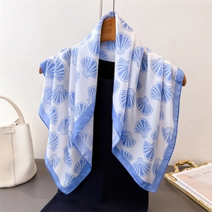 Elegant silk scarf with blue ocean shell print draped on a wooden hanger with bag