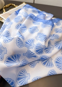 Close-up of blue shell print on white silk-like scarf with elegant blue border detail