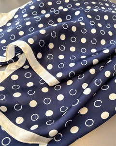 Macro detail of silk scarf featuring dark blue polka dot print and glossy satin hem