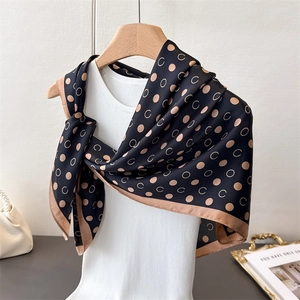 Detail of silk scarf with golden dots and C patterns on a white knitted top