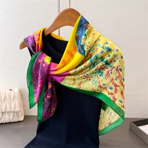 Elegant peacock print satin silk square scarf draped on a wooden hanger with vibrant colors