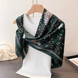 Elegant dark green satin scarf with ethnic animal prints draped on a white knit vest