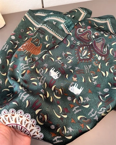 Close-up of dark green satin scarf with intricate elephant patterns and H letter motifs