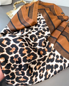 Détail du foulard en satin de soie avec imprimé léopard et rayures sur un plateau doré