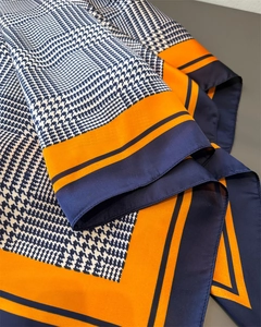 Detailopname van een zijden sjaal met pied-de-poule patroon en oranje blauwe randen