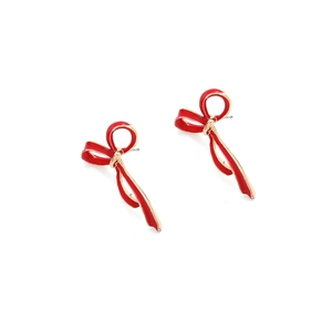 Dettaglio di orecchini a fiocco in smalto rosso con base dorata su sfondo bianco puro
