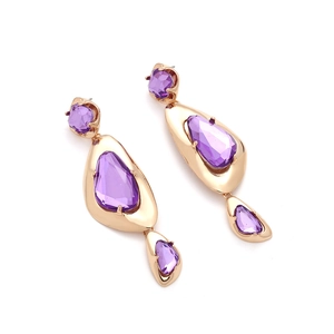 Detailed view of long gold drop earrings with geometric faceted purple gemstones