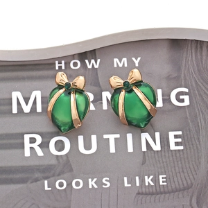 Macro detail of green enamel heart earrings with gold bow and emerald-tone center stone