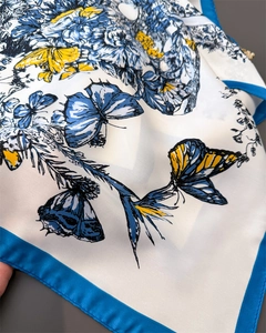 Gros plan du foulard en soie montrant des fleurs, des papillons et des bords bleus