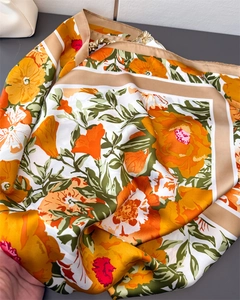Detailed texture of a floral silk scarf featuring vibrant orange flowers and gold borders