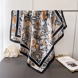 Elegant oversized floral silk scarf in caramel and grey tones draped over a minimalist stand