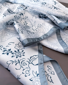 Close-up of silk-like scarf featuring blue floral ink prints and gray satin edge detail