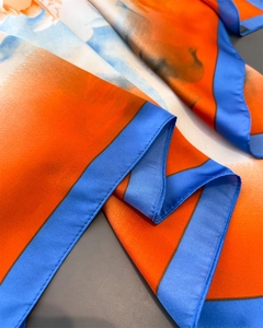 Detail of silk-like scarf featuring vibrant orange and blue floral patterns and stitching