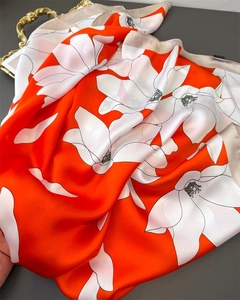 Close-up of elegant orange silk scarf featuring white floral patterns on satin fabric