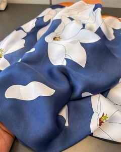 Macro detail of glossy blue satin scarf with white floral print and orange hem