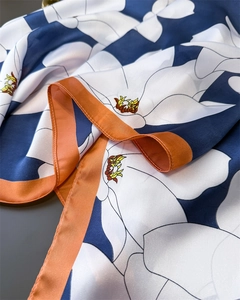 Detail of elegant satin scarf showing white floral print on navy silk and orange hem