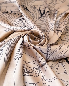 Detailed view of champagne satin fabric featuring minimalist black floral art sketches