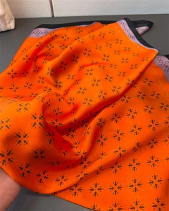 Detailstruktur des orangen Seidenschals mit schwarzem Kreuzmuster und lila Randverzierung
