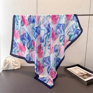 Elegant floral satin silk square scarf with pink lilies and blue borders on a display stand