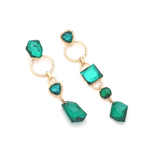Macro view of gold-tone earrings with emerald green crystals and geometric shapes