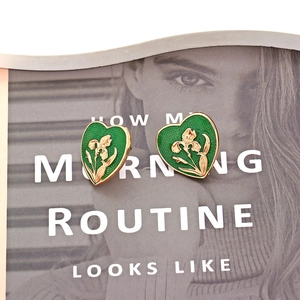 Detail of vintage heart earrings with green enamel and gold floral embossing on a magazine