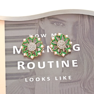 Vintage gold earrings with green enamel floral design and pearls on a magazine