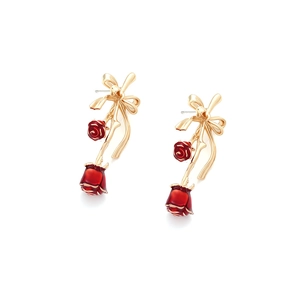 Close-up of red enamel rose earrings with golden bows on a white background