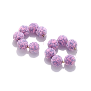 Close-up of C-shaped hoop earrings with purple and pink faux fur pom-poms and gold beads