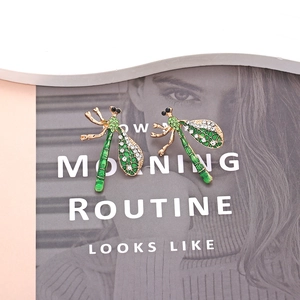 Detailed close-up of dragonfly stud earrings with green enamel and white rhinestones