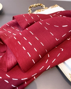 Close-up of red herringbone woven scarf with white stitched lines on a gold tray