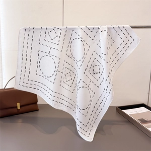 Minimalist white silk scarf with black geometric patterns draped on a metal rod