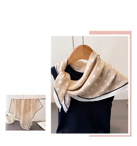 Detailed close-up of beige polka dot silk scarf with elegant black stitched edges