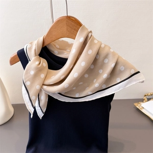Detailed close-up of beige polka dot silk scarf draped on a wooden hanger with trim detail