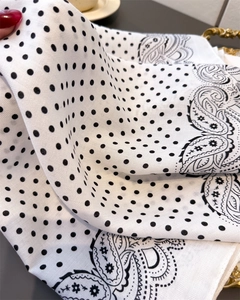 Detail of silk-like white scarf featuring classic black polka dots and paisley patterns