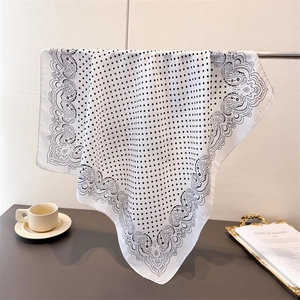 Close-up of black paisley and polka dot patterns on a white silk-like square scarf