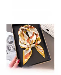 Détail d'un foulard en soie aux motifs de feuilles orange et jaune sur un sac à main blanc