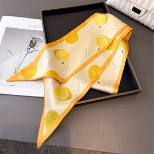 Détail d'un foulard en soie jaune avec motif durian mignon plié sur un plateau noir