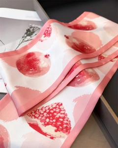 Détail d'un foulard en soie avec imprimé grenade et bords roses sur plateau gris