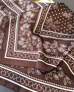 Macro detail of dark coffee silk scarf with white floral paisley prints and smooth satin texture