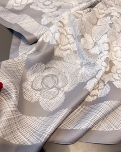 Close-up of grey silk-like square scarf with white camellia floral print and soft texture