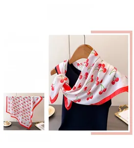 Detail of white silk scarf showing vibrant red cherry print and high-quality red hem