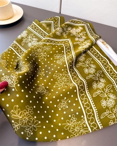 Close-up of olive green silk square scarf featuring elegant polka dots and floral patterns