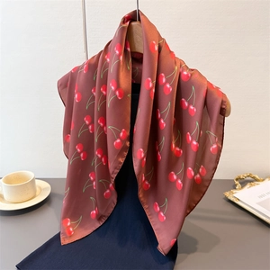 Brown satin square scarf with red cherry prints hanging on a wooden hanger gracefully