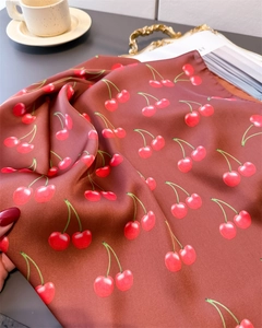 Close-up of silk-like square scarf with cherry print on a retro tray and coffee cup